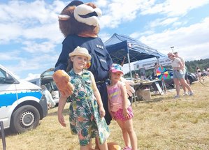 policyjna maskotka lew na imprezie plenerowej obok której stoją dwie dziewczynki