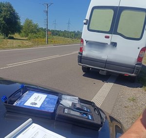 na drodze zaparkowany bus w tle policjant wprowadzający dane na urządzeniu oraz protokół