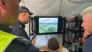 policjanci oraz operator drona przy wyświetlonym obrazie ukazującym widok uroczystości z góry wokół pomnika w postaci orła zgromadzeni licznie ludzie