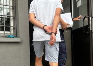 mężczyzna idzie po schodach w kajdankach przed nim policjant