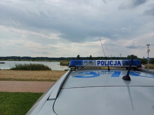 policjanci na łodzi motorowej na wodzie patroluja teren zbiornika wodnego na brzegu którego wypoczywają osoby