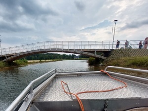 policjanci na łodzi motorowej na wodzie patroluja teren zbiornika wodnego na brzegu którego wypoczywają osoby