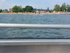 policjanci na łodzi motorowej na wodzie patroluja teren zbiornika wodnego na brzegu którego wypoczywają osoby