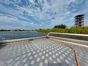 policjanci na łodzi motorowej na wodzie patroluja teren zbiornika wodnego na brzegu którego wypoczywają osoby