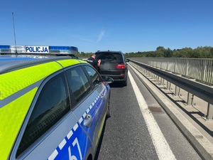 radiowóz policyjny na drodze przed nim samochód osobowy koloru czarnego który pcha do przodu policjant pora letnia