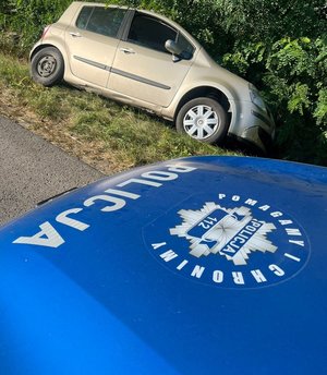pojazd osobowy w przydrożnym rowie leży na boku widoczny fragment przodu radiowozu na masce którego jest napis pomagamy i chronimy oraz napis policja i policyjna gwiazda