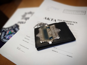 policyjna legitymacja leży na aktach sprawy w tle emblemat z napisem policja