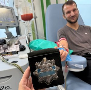 mężczyzna leży na fotelu medycznym do ręki ma podpięte medyczne wenflony w tle osoba trzyma policyjną odznakę z napisem policja 
Zdjęcie wykonania Krzysztof Luchowski