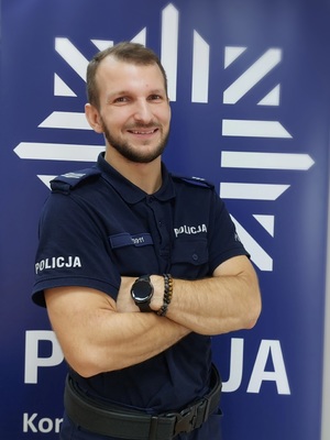 policjant stoi na tle granatowego baneru na którym jest policyjna biała gwiazda