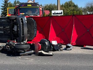 miejsce zdarzenia drogowego samochód osobowy oraz motocykl leżą na boku na jezdni w tle pojazd straży pożarnej oraz strażacki parawan
