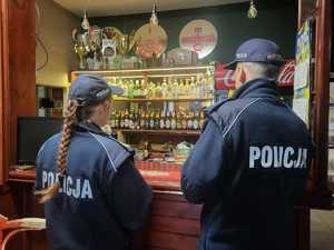 Policjantka i policjant stoją przed ladą i przeprowadzają kontrolę.