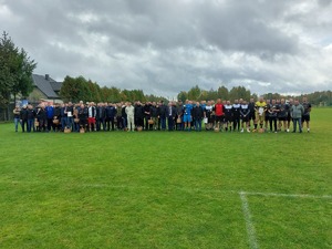 Wszyscy uczestnicy turnieju na tle boiska do gry w piłkę.