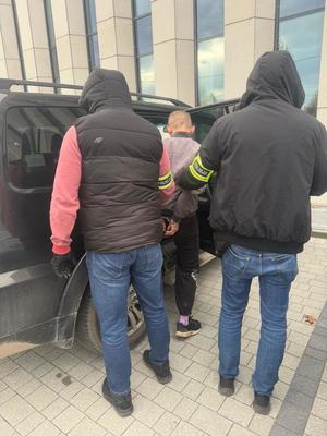 Policjanci prowadzą zatrzymanego mężczyznę do radiowozu