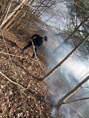 na zdjęciu widoczny jest policjant gaszący płonącą trawę