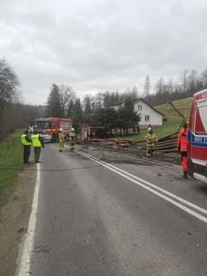 zdjęcia ze zdarzenia drogowego w Boguszówce. na drodze stoi dwóch umundurowanych policjantów , w tle samochód ciężarowy przewrócony w rowie i rozsypane drewno na poboczu drogi