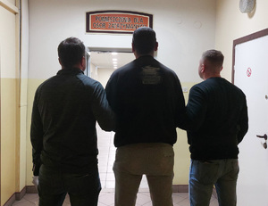 dwóch nieumundurowanych policjantów prowadzi zatrzymanego mężczyznę w korytarzu komendy