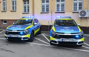Dwie Kie Sportage postawione przed budynkiem komendy z włączonymi sygnałami świetlnymi