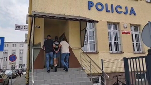 Policjanci prowadzą zatrzymanego po schodach do budynku komendy