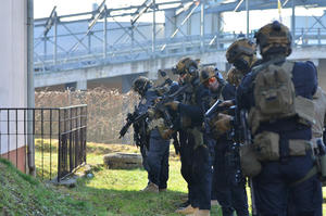 Na zdjęciu widać policjantów z grupy kontrterrorystycznej z Rzeszowa podczas ćwiczeń w Sanoku. Policjanci są wyposażeni w sprzęt specjalistyczny. Widać również nieumundurowanych policjantów sanockiego wydziału kryminalnego. Przemieszczają się z pistoletami w rękach udzielając sobie wzajemnej asysty.