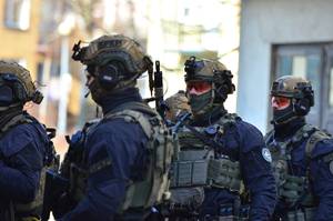 Na zdjęciu widać policjantów z grupy kontrterrorystycznej z Rzeszowa podczas ćwiczeń w Sanoku. Policjanci są wyposażeni w sprzęt specjalistyczny. Widać również nieumundurowanych policjantów sanockiego wydziału kryminalnego. Przemieszczają się z pistoletami w rękach udzielając sobie wzajemnej asysty.