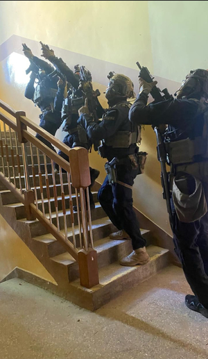 Na zdjęciu widać policjantów z grupy kontrterrorystycznej z Rzeszowa podczas ćwiczeń w Sanoku. Policjanci są wyposażeni w sprzęt specjalistyczny. Widać również nieumundurowanych policjantów sanockiego wydziału kryminalnego. Przemieszczają się z pistoletami w rękach udzielając sobie wzajemnej asysty.