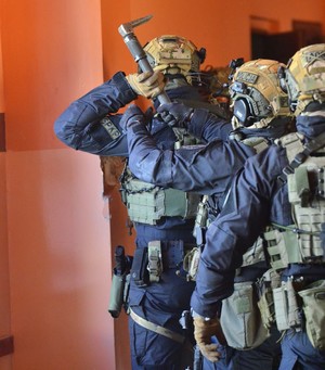 Na zdjęciu widać policjantów z grupy kontrterrorystycznej z Rzeszowa podczas ćwiczeń w Sanoku. Policjanci są wyposażeni w sprzęt specjalistyczny. Widać również nieumundurowanych policjantów sanockiego wydziału kryminalnego. Przemieszczają się z pistoletami w rękach udzielając sobie wzajemnej asysty.