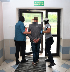 Zatrzymany mężczyzna prowadzony przez policjantów.