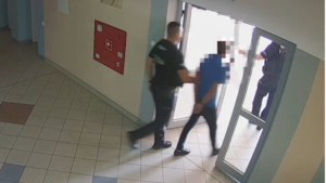 Policjanci wyprowadzają z budynku mężczyznę z założonymi kajdankami.