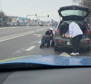 Umundurowany policjant pomagający w wymianie niesprawnego koła w samochodzie.