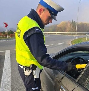 Na zdjęciu umundurowany policjant przeprowadzający badanie trzeźwości u kierującego samochodem.