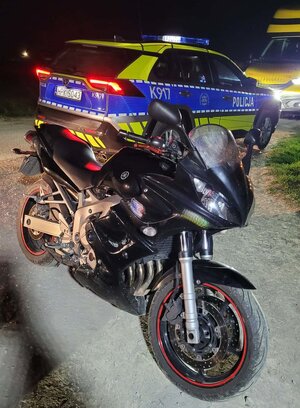 Na zdjęciu zatrzymany przez policjantów motocykl Yamaha. Pojazd jest na samochodzie holowniczym. Na zdjęciu widać również umundurowanego policjanta. Jest noc. Tło jest ciemne.