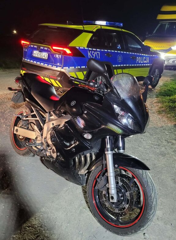 Na zdjęciu zatrzymany przez policjantów motocykl Yamaha. Pojazd jest na samochodzie holowniczym. Na zdjęciu widać również umundurowanego policjanta. Jest noc. Tło jest ciemne.