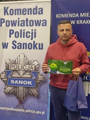 Na zdjęciu mężczyzna- asp. szt. Paweł Prodziewicz trzymający w ręce dyplom za zajęcie trzeciego miejsca. w Tle baner z napisem Komenda Powiatowa Policji w Sanoku.