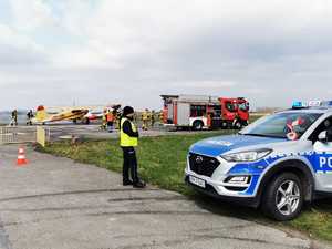 Na pierwszym planie radiowóz i policjantka, w tle miejsce zdarzenia.