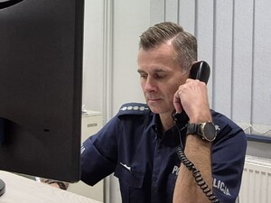 Policjant siedzący za komputerem i trzymający w ręku słuchawkę telefonu