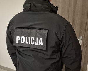 Zdjęcie policjanta operacyjnego w kurtce z napisem POLICJA